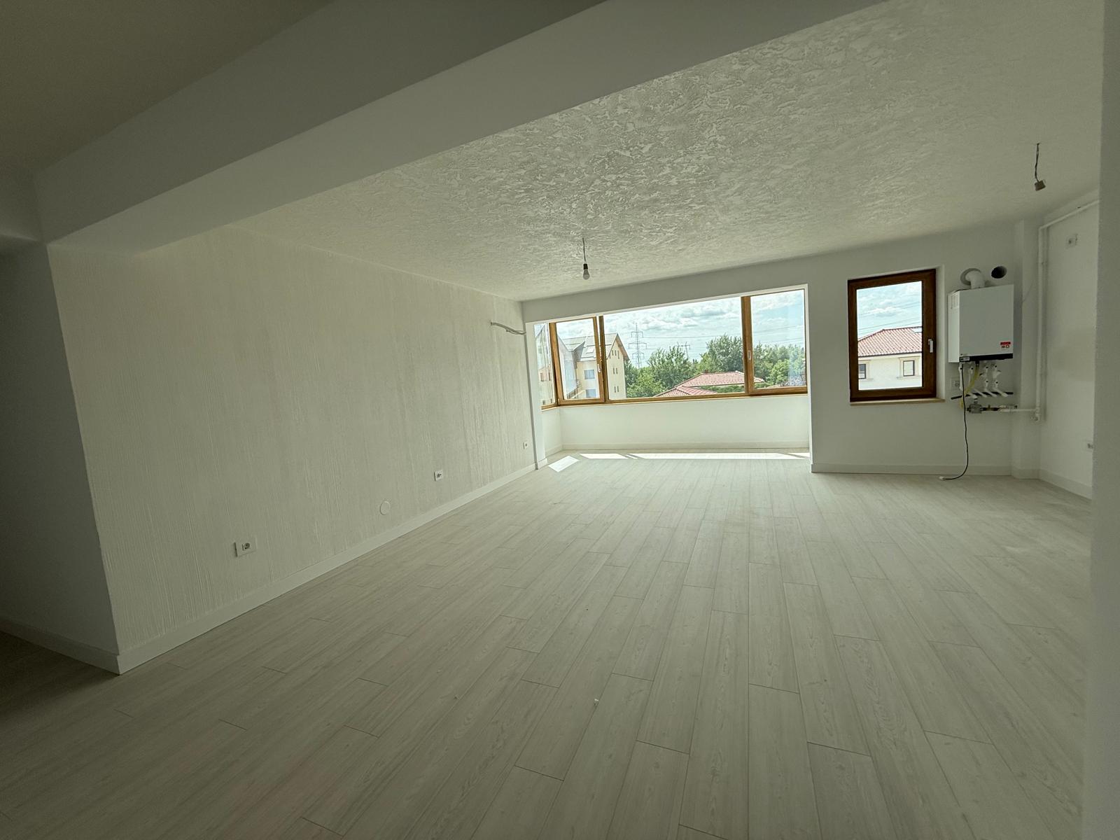 Living open-space cu parchet gri, ferestre mari din lemn și centrală pe perete