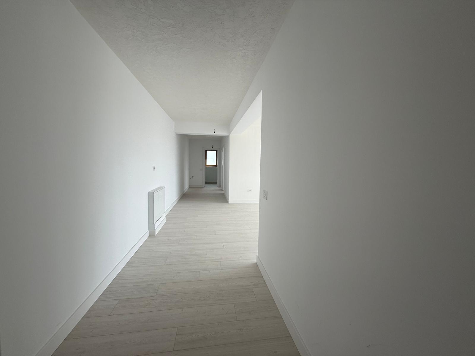 Hol coridor lung cu parchet gri deschis, calorifer alb și lumină naturală de la capăt