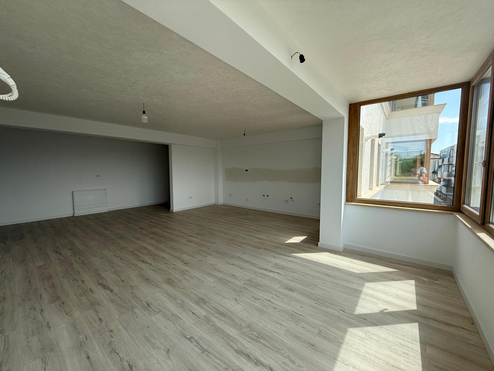 Living open-space cu ferestre mari din lemn, grindă aparentă și parchet deschis