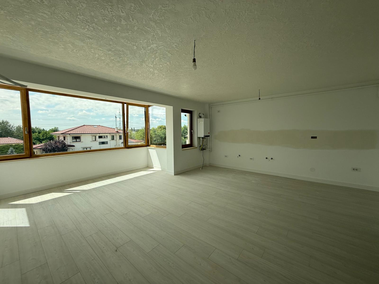 Living/kitchenette cu parchet gri, ferestre din lemn și racorduri tehnice pe perete