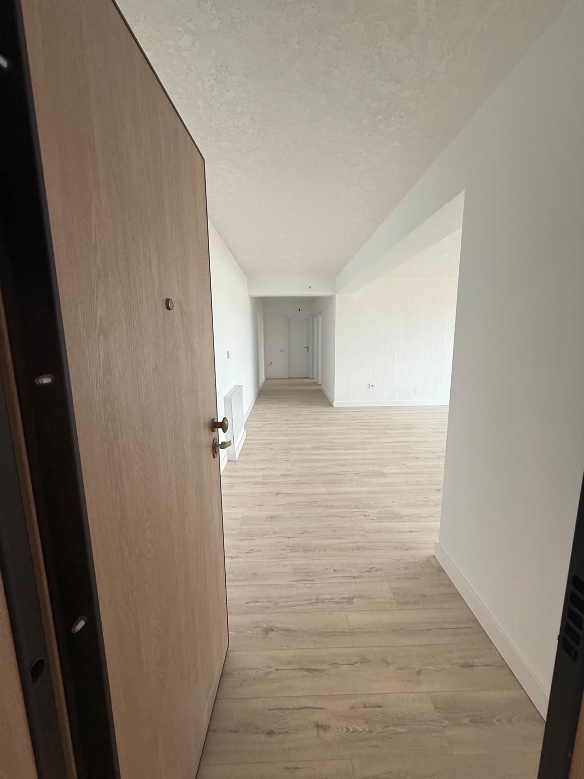 Intrare în apartament cu ușă din lemn, hol lung spre living și lumină naturală din dreapta