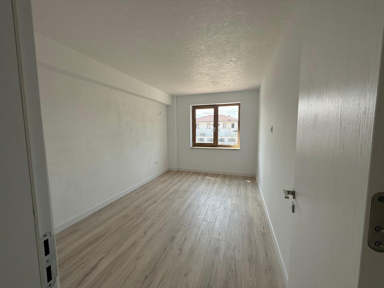 Living luminos cu fereastră mare din lemn și vedere spre clădirile învecinate