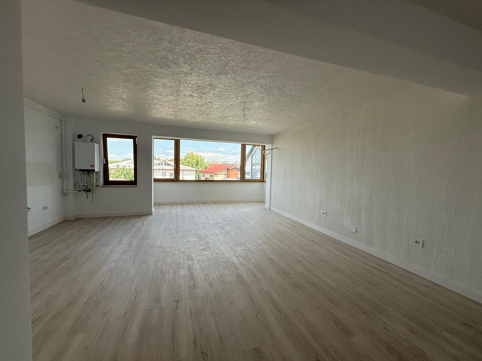 Living open-space cu parchet deschis, fereastră mare din lemn și centrală pe perete