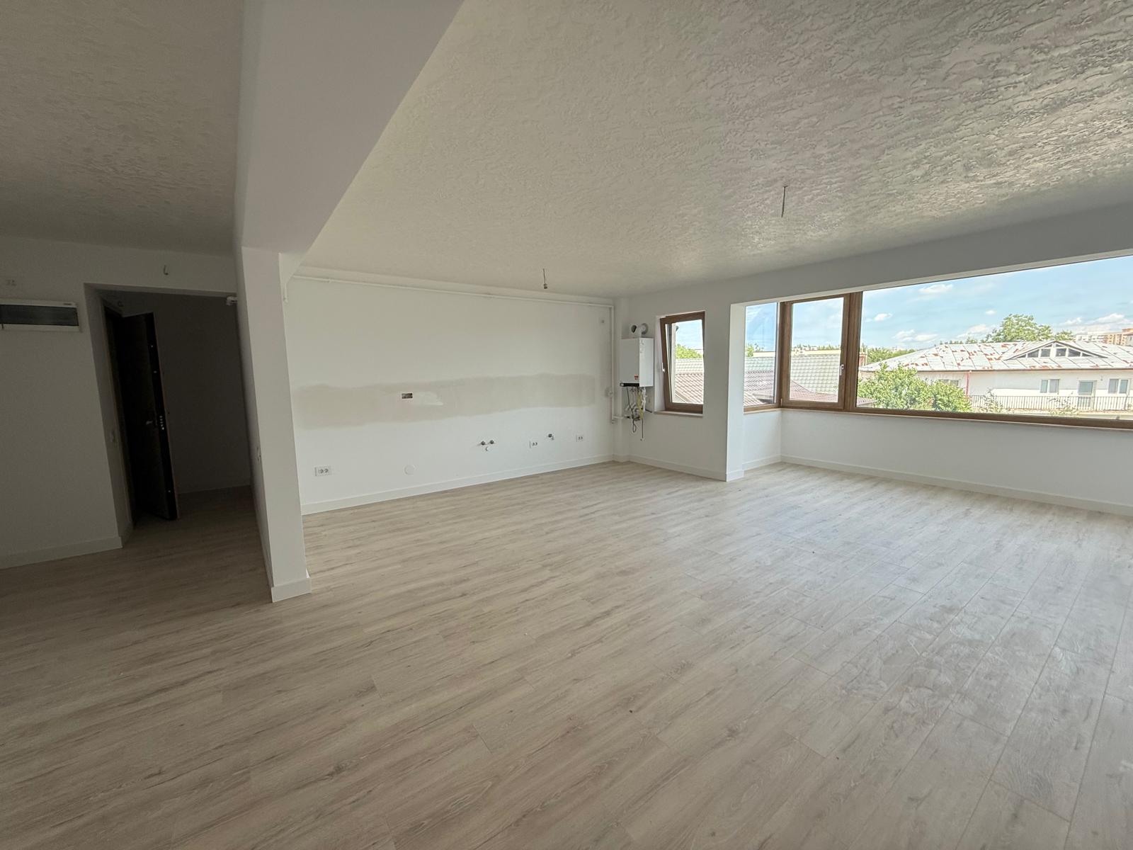 Living open-space cu parchet deschis, fereastră din lemn și racorduri tehnice pe perete