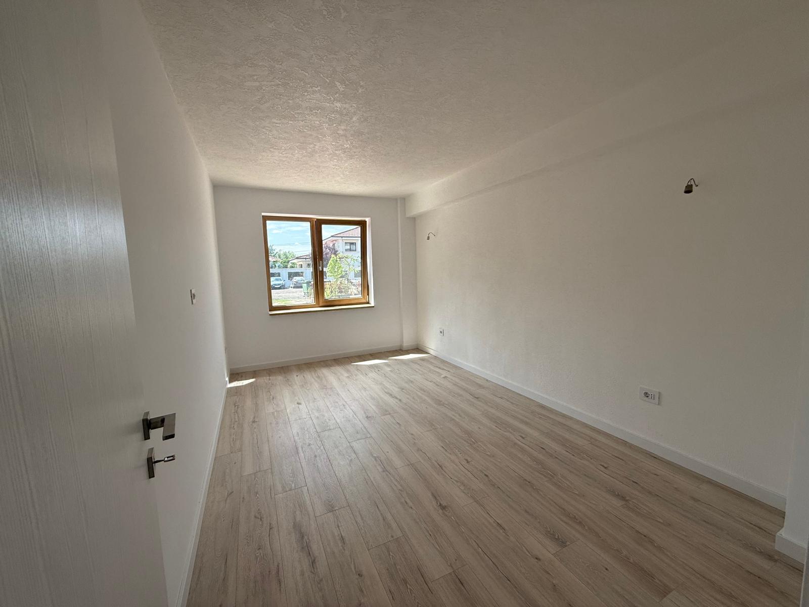 Dormitor luminos cu parchet deschis și fereastră din lemn spre verdeată