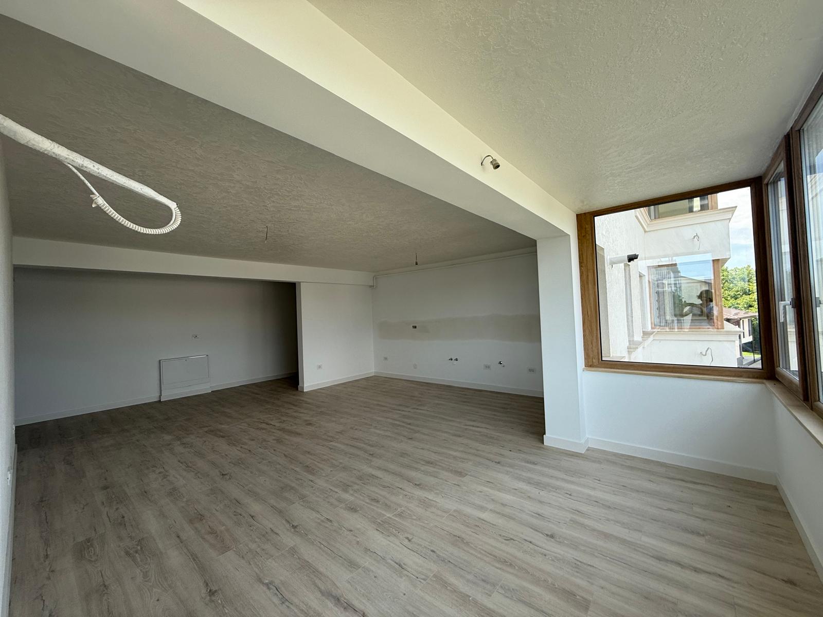 Living open-space cu parchet deschis, fereastră din lemn și grindă structurală aparentă