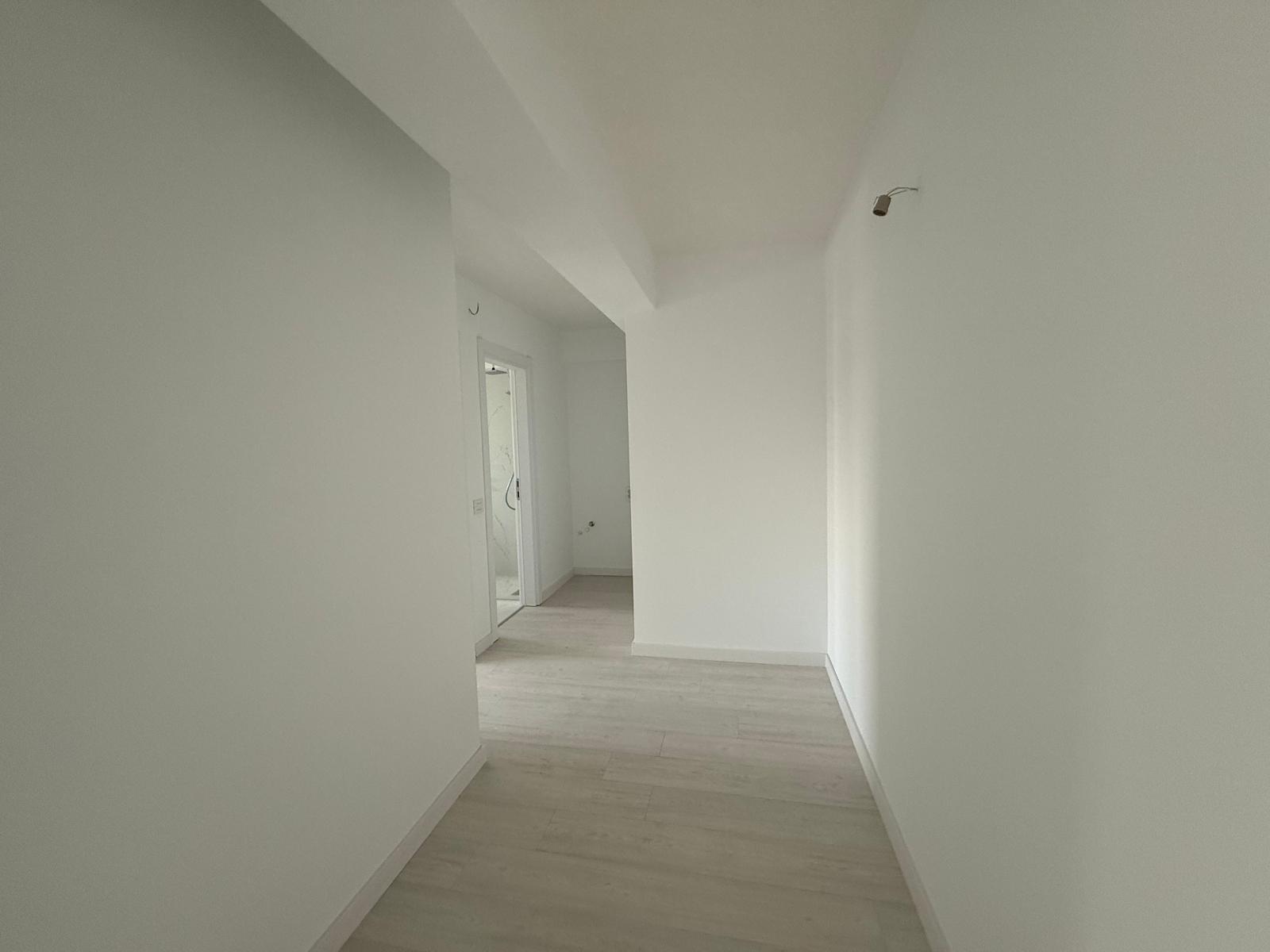 Hol interior luminos cu pereți albi, parchet deschis și corp de încălzire