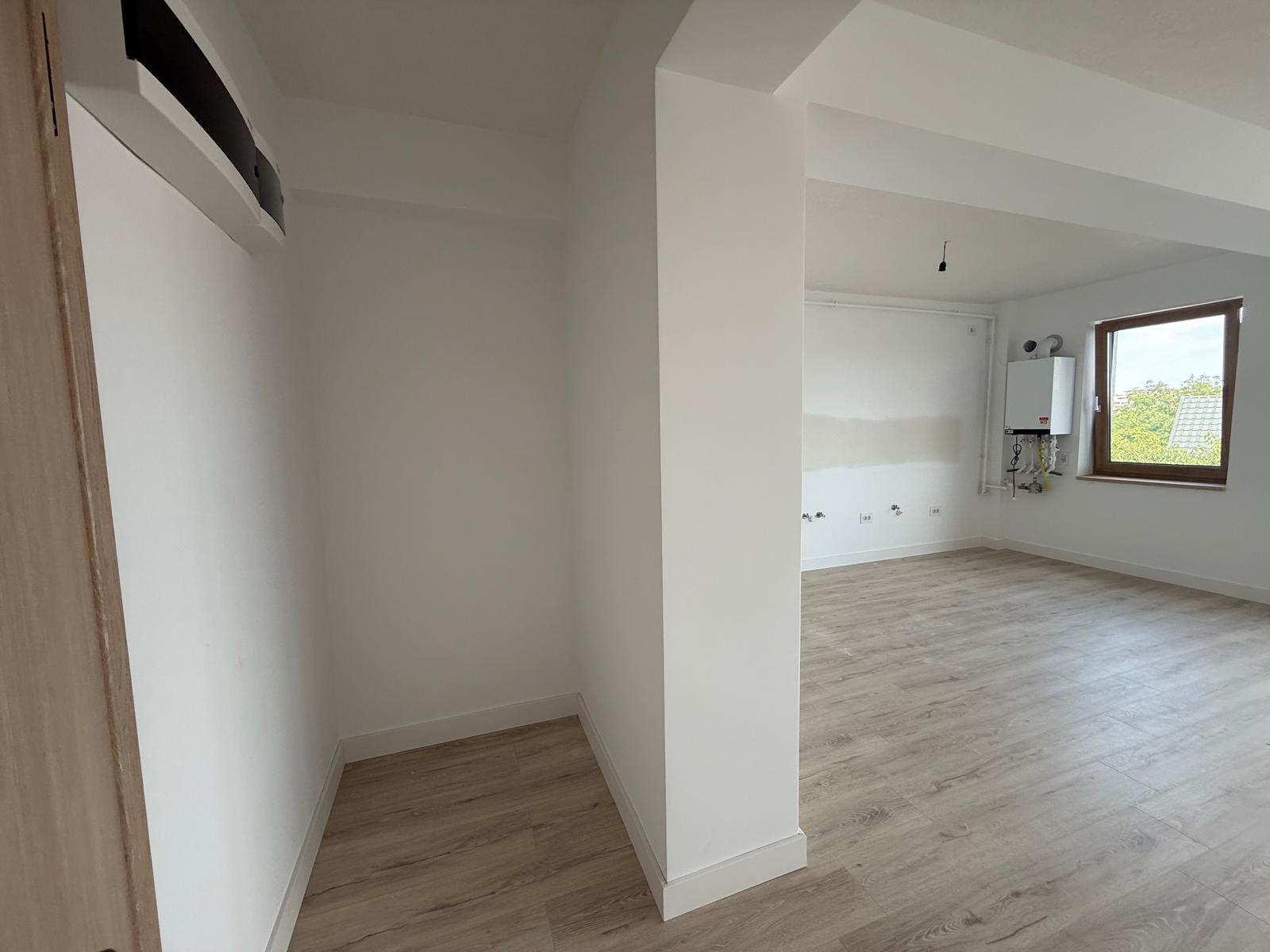 Zonă kitchenette cu parchet, fereastră din lemn, centrală pe perete și racorduri de apă