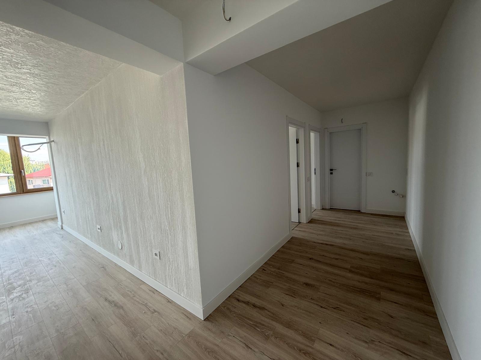 Zonă de living și hol cu parchet deschis, fereastră din lemn și perete texturat cu prize
