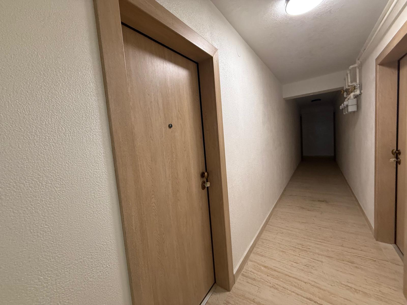 Hol coridor cu uși din lemn deschis, pardoseală cu dale și corp de iluminat rotund