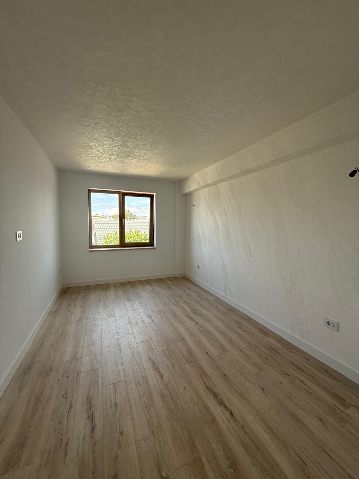 Dormitor cu parchet deschis, fereastră din lemn și perete cu textură decorativă