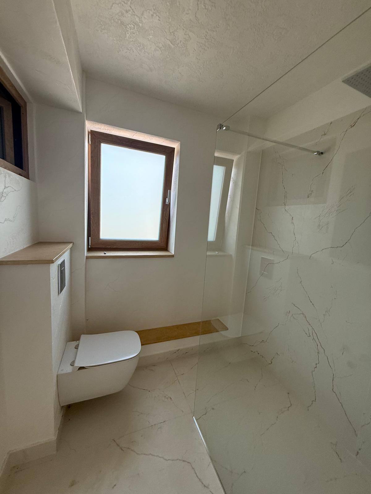 Baie modernă cu duș walk-in, toaletă suspendată, geam mat cu ramă din lemn și finisaje marmură